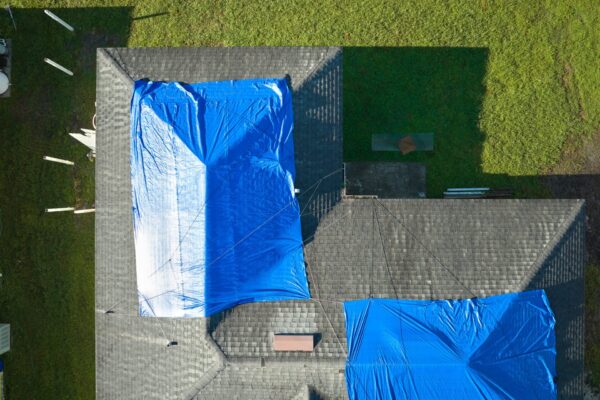 Top view of leaking house roof covered with protective tarp sheets against rain water leaks until replacement of asphalt shingles in Lewiston, ID.