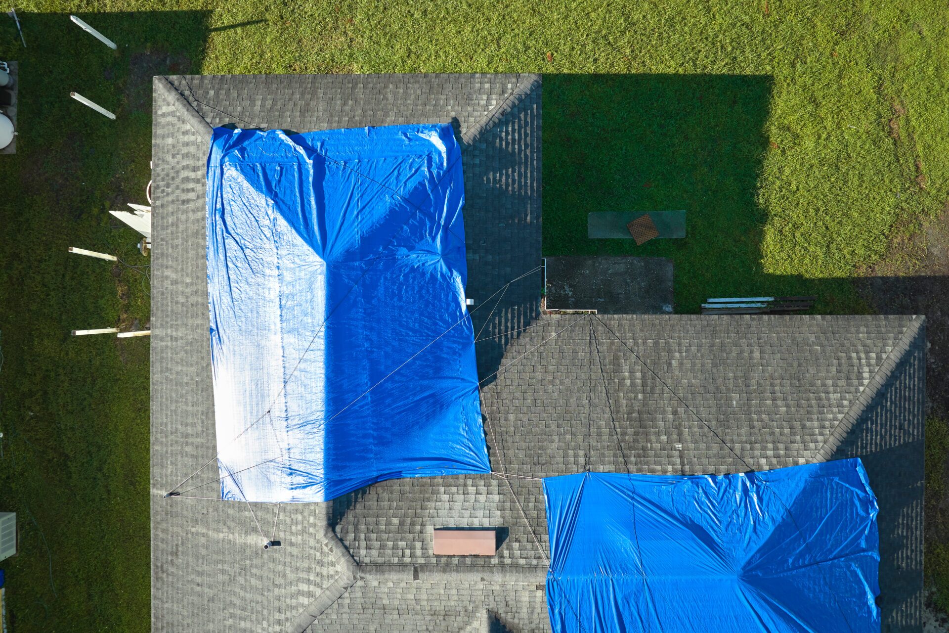 Top view of leaking house roof covered with protective tarp sheets against rain water leaks until replacement of asphalt shingles in Lewiston, ID.