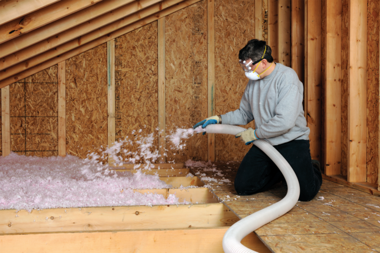 Roofing professional blowing pink insulation into an attic space.